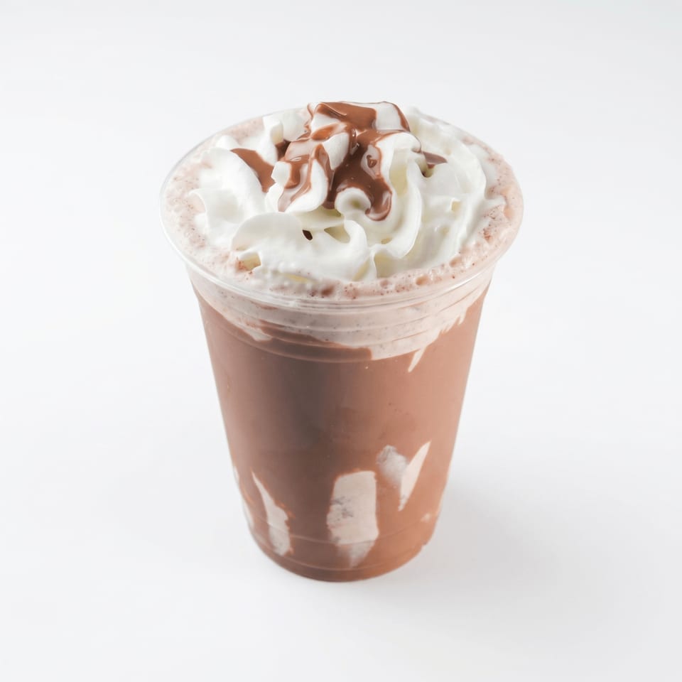 Chocolate milkshake in a clear plastic cup, topped with whipped cream and chocolate syrup.