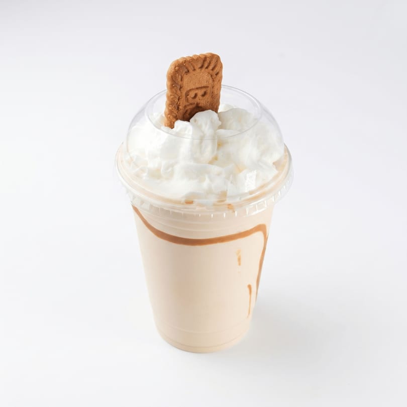 A caramel milkshake with whipped cream and a Biscoff cookie in a clear plastic cup.
